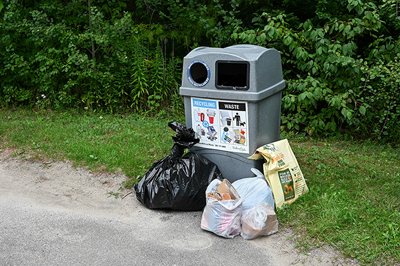 Image of waste container surrounded by garbage bags